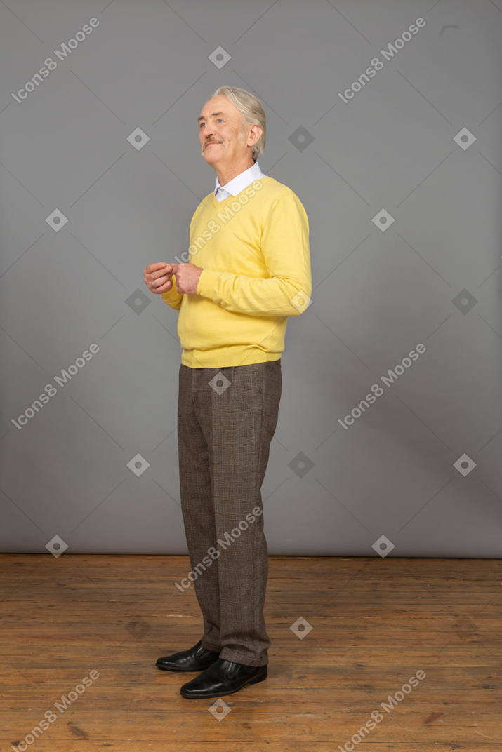 Vista de tres cuartos de un anciano con un jersey amarillo juntando las manos y mirando a un lado