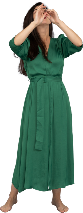 手を上げながらフルートを演奏する緑のドレスを着た若い女性の正面図