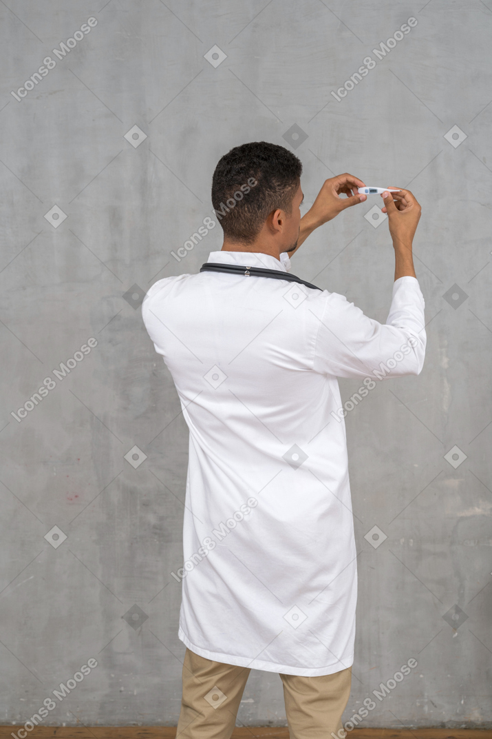 Rückansicht eines männlichen arztes, der ein thermometer hält