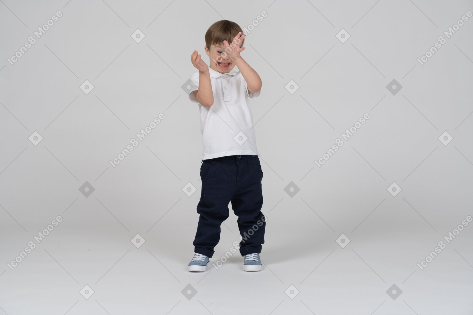 Vista frontal de um menino escondido atrás de suas mãos com um sorriso
