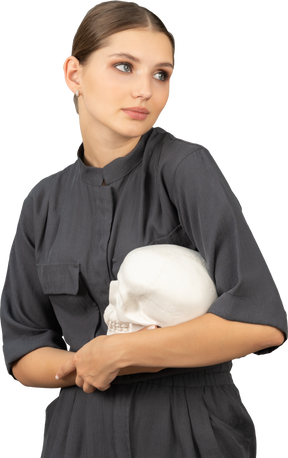 Front view of a young woman in a jumpsuit holding a plaster skull