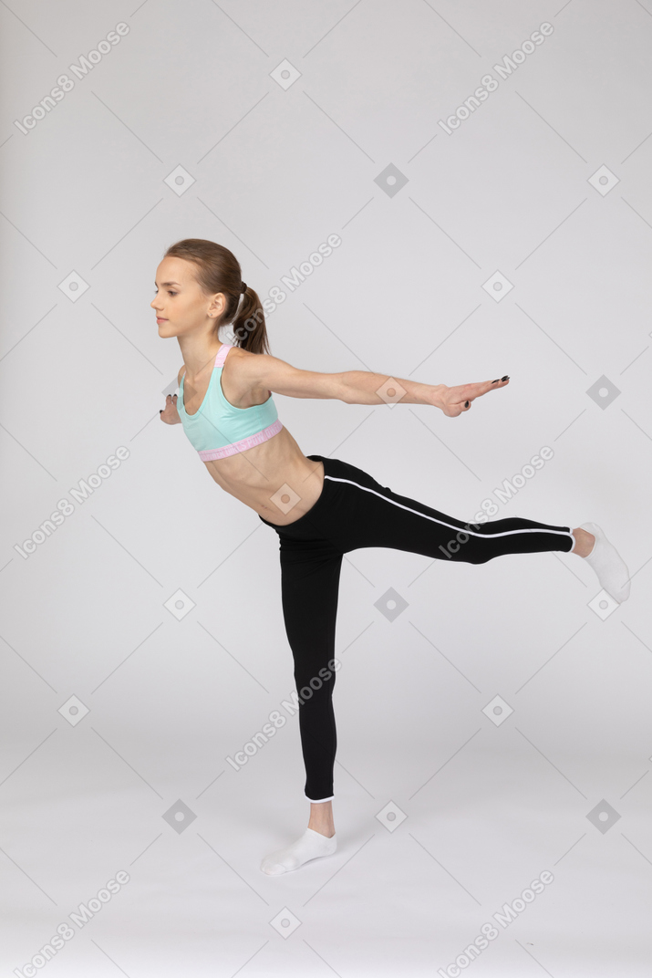 Vista de tres cuartos de una jovencita en ropa deportiva de equilibrio sobre su pierna