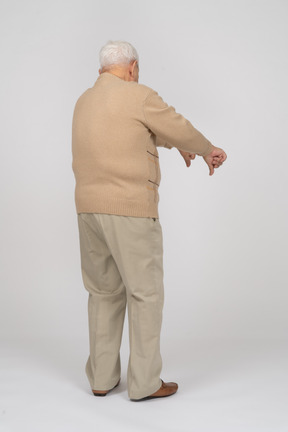 Vista trasera de un anciano con ropa informal que muestra los pulgares hacia abajo