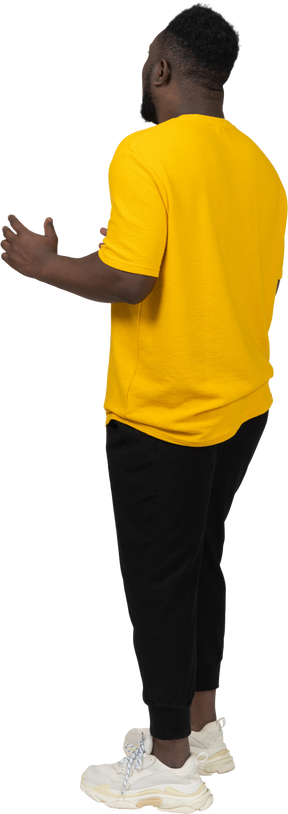 뭔가를 설명하는 노란색 티셔츠를 입고 몸짓을 하는 짙은 피부의 젊은 남자의 3/4 뒷모습