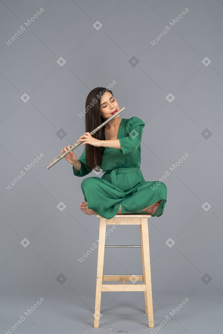 播放单簧管的年轻女士的全长，她的双腿交叉在木椅上
