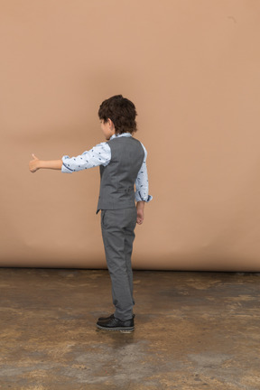 Вид сбоку на мальчика в сером костюме, показывающего большой палец вверх