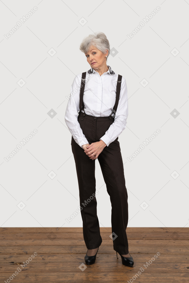 Front view of a displeased old lady in office clothing holding hands together