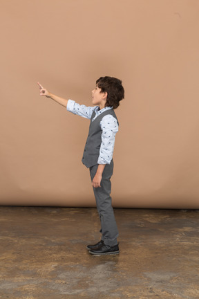 Vista lateral de un niño con traje gris señalando