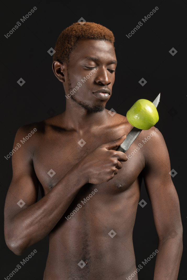 A muscular young man holding a knife with a green apple on it