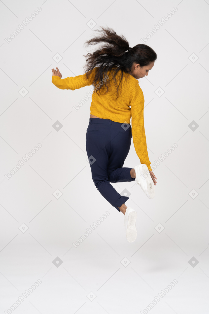 Retrovisor de uma garota com roupas casuais pulando e tentando tocar o pé