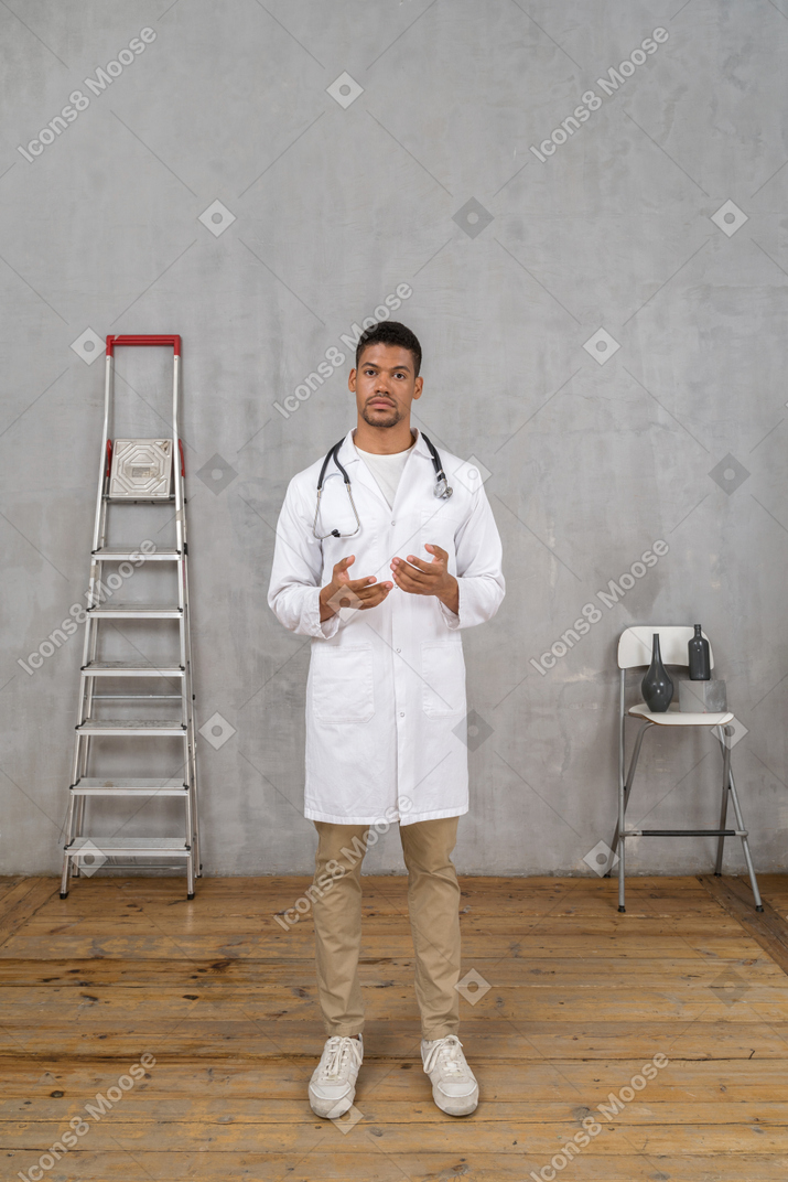 사다리와 의자가 뭔가를 설명하는 방에 서있는 젊은 의사의 전면보기