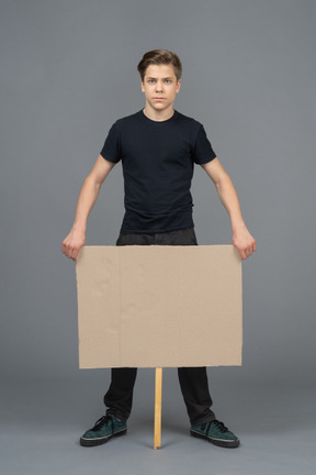 Joven serio de pie con un cartel en blanco