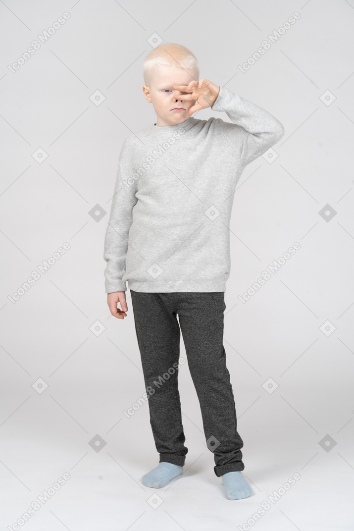 Front view of a grimacing kid boy touching nose