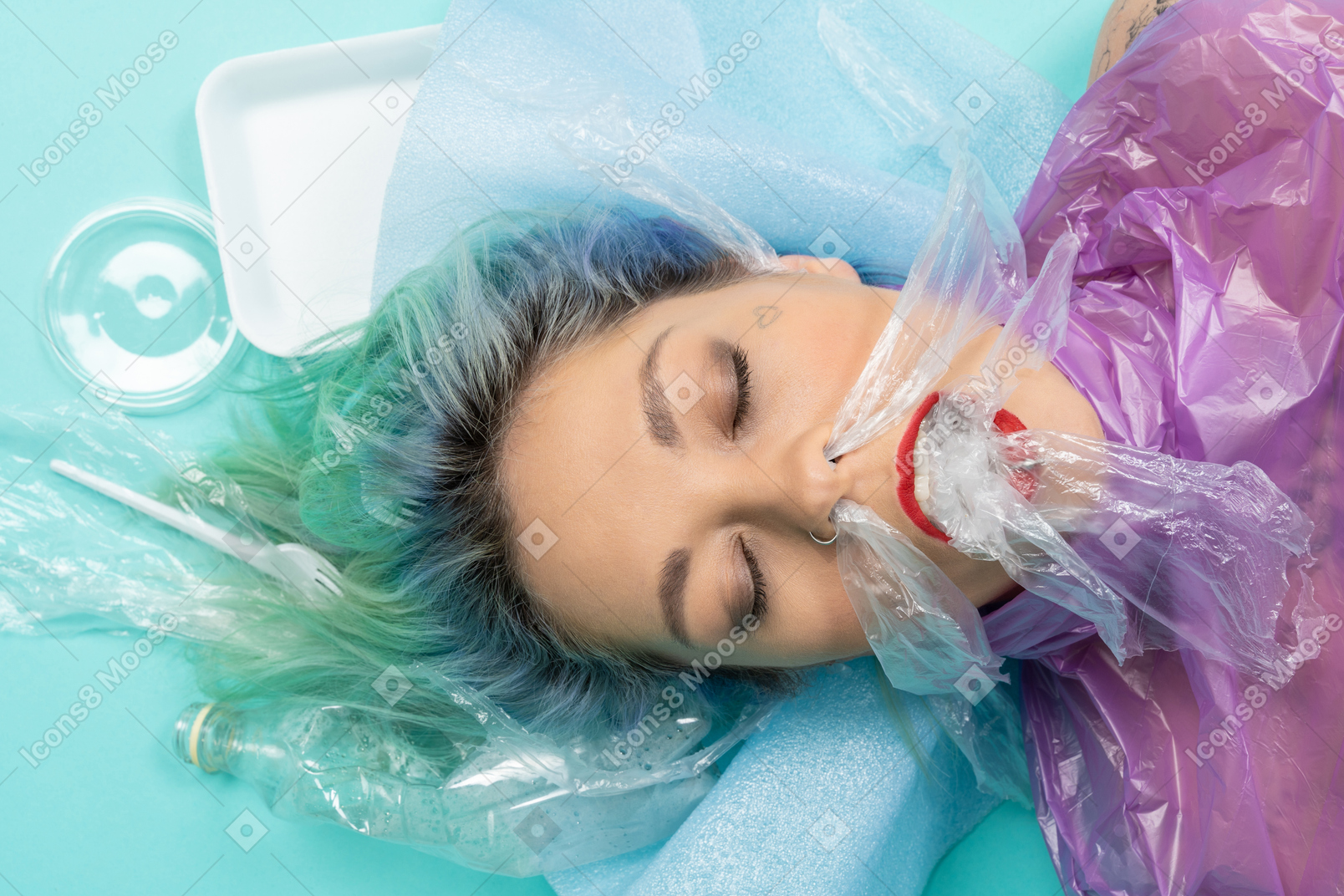 Jovem mulher deitada com os olhos fechados, rodeada de muitas coisas de plástico