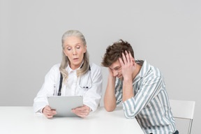 Пожилая женщина-врач показывает пациенту что-то на своем цифровом планшете