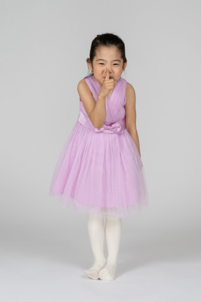 Portrait of a little girl in a pretty dress showing silence sign