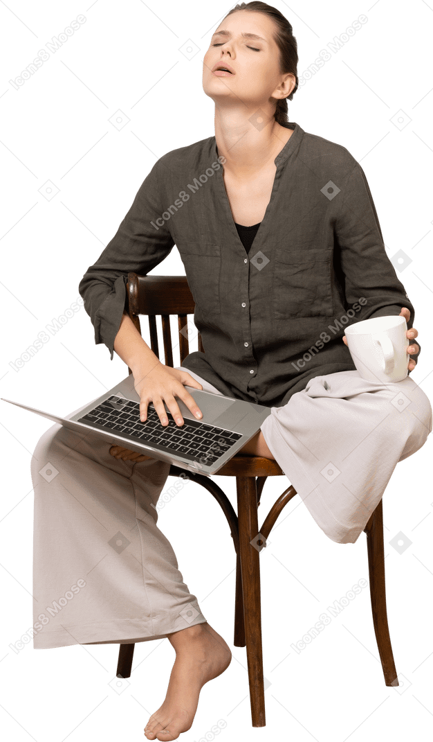 Вид спереди уставшей молодой женщины в домашней одежде, сидящей на стуле с ноутбуком и чашкой кофе