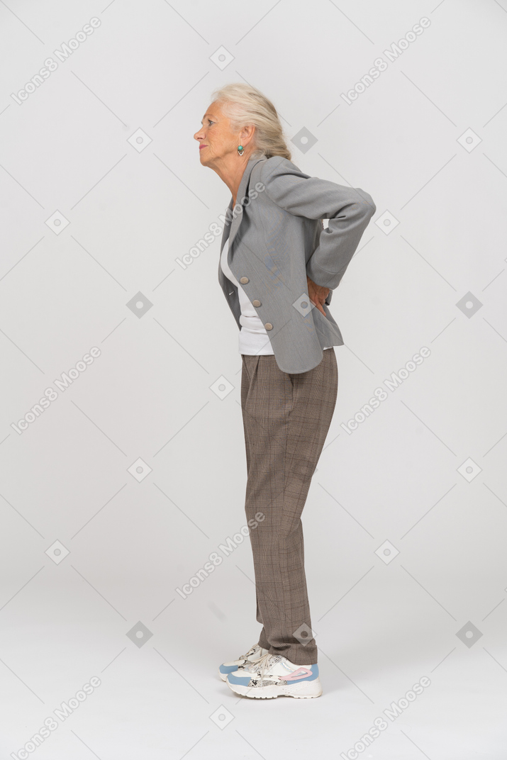 Vista laterale di una vecchia signora in abito che soffre di dolore alla schiena