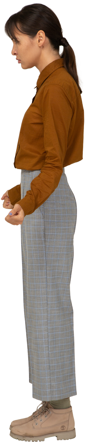 Вид сбоку молодой азиатской женщины в бриджах и блузке, сжимающей кулаки