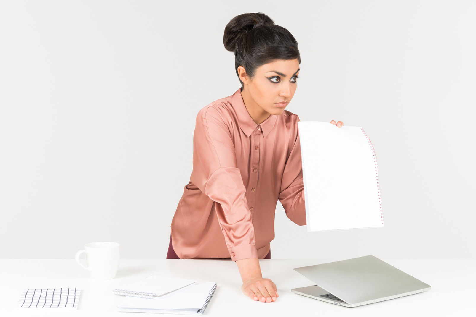 Displeased young indian office worker standing at the office desk and showing paper