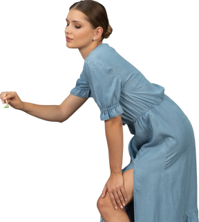 一个穿着蓝色连衣裙的年轻女子拿着牙刷向前倾的侧视图