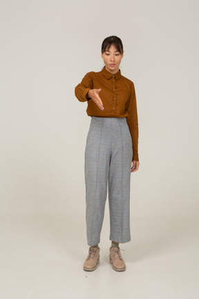 Front view of a greeting young asian female in breeches and blouse outstretching hand