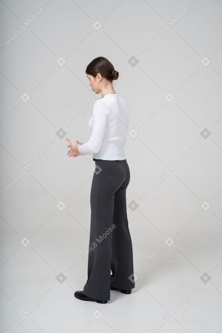 Молодая женщина в черных брюках и белой блузке стоит в профиль