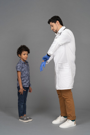Doctor poniéndose guantes quirúrgicos mientras chico busca