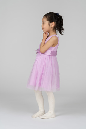Маленькая девочка в розовом платье мечтательно смотрит в сторону