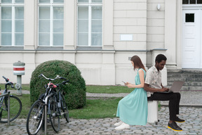 A man and woman sitting on a suitcase near a building