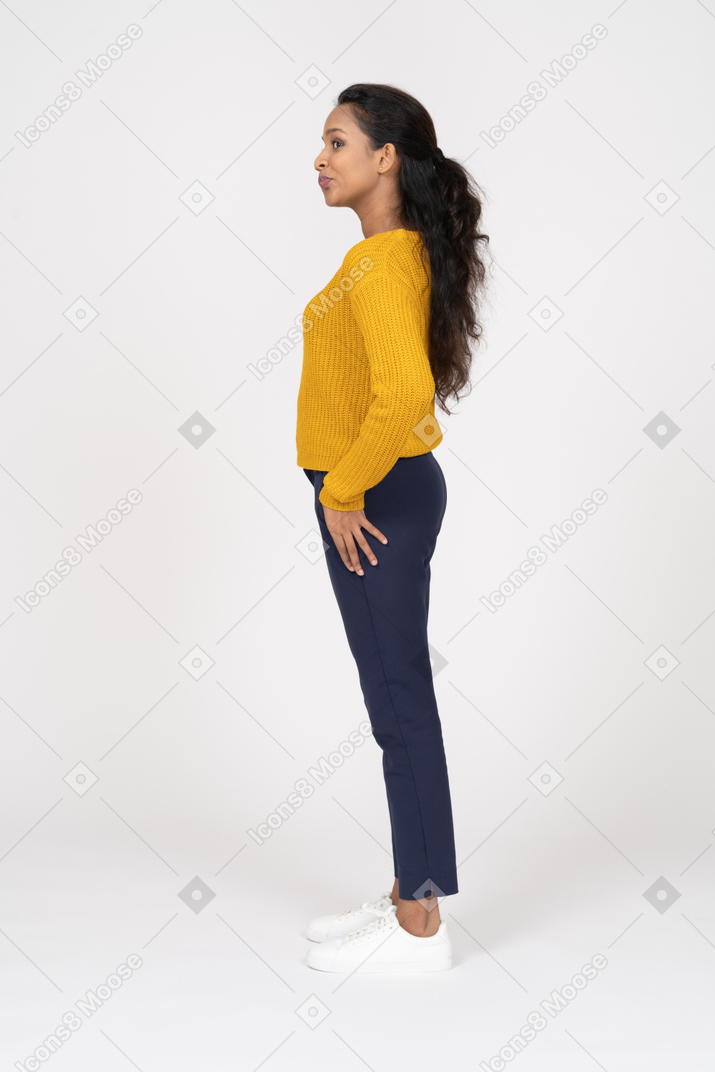 Vista laterale di una ragazza in abiti casual in piedi con la mano sull'anca