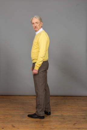 Seitenansicht eines unzufriedenen alten mannes in einem gelben pullover, der kamera betrachtet