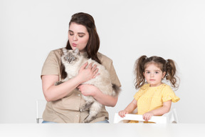 Maman assise à côté d'une fille dans la chaise pour enfants et tenant un chat