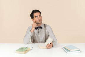 Pensive adult student sitting at the table with opened book