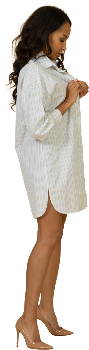 Vista laterale di una giovane femmina dalla carnagione scura che abbottona il suo vestito bianco