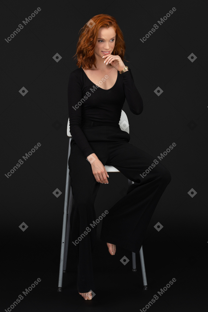 검은 옷을 입고 키가 큰 회색 의자에 앉아 있는 젊은 여성