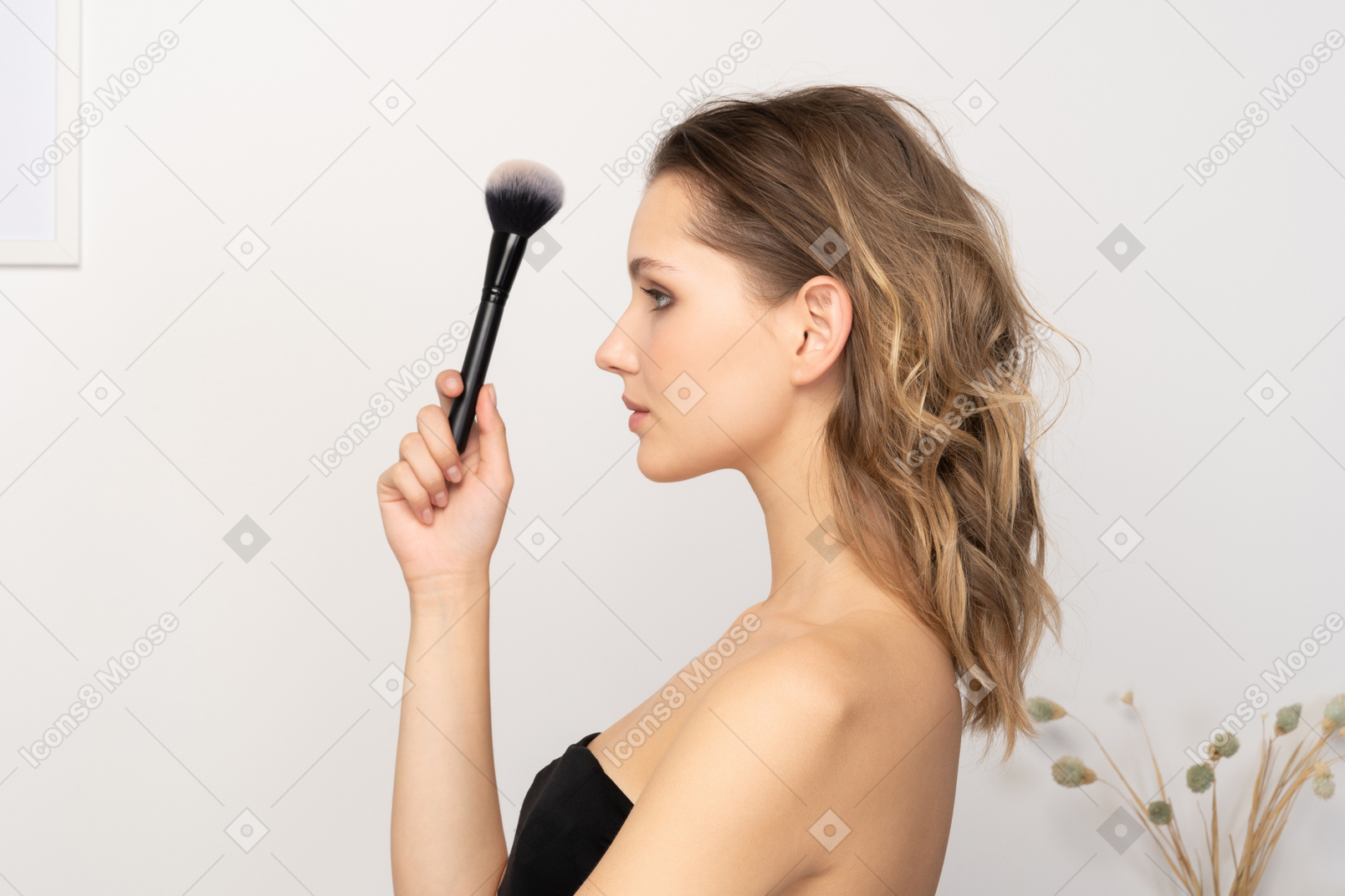 Vista lateral de uma jovem sensual segurando um pincel de maquiagem