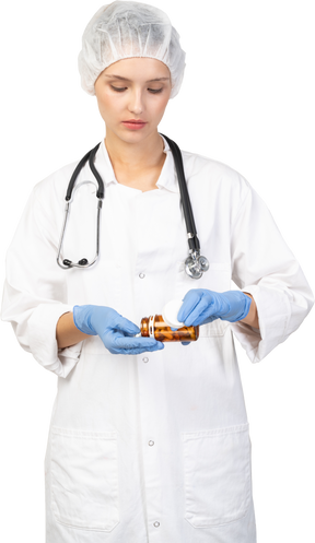 Vista frontale di una giovane dottoressa che versa pillole dal barattolo