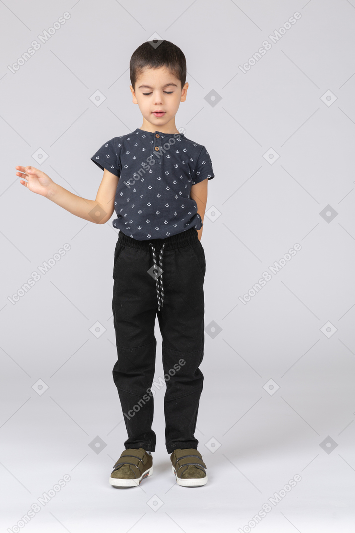 Front view of a cute boy standing with closed eyes and waving