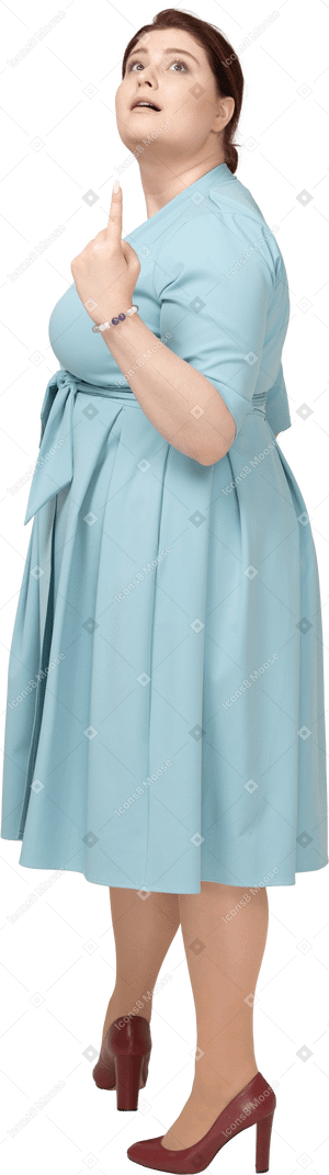Vista lateral de una mujer en vestido azul apuntando hacia arriba con un dedo