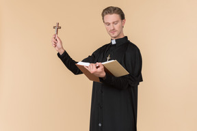 Catholic priest holding cross and reading a bible