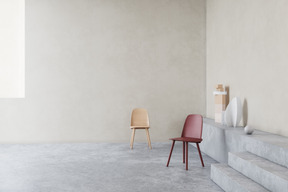 Two colorful chairs standing on a stone-like floor in a very grey minimalist room