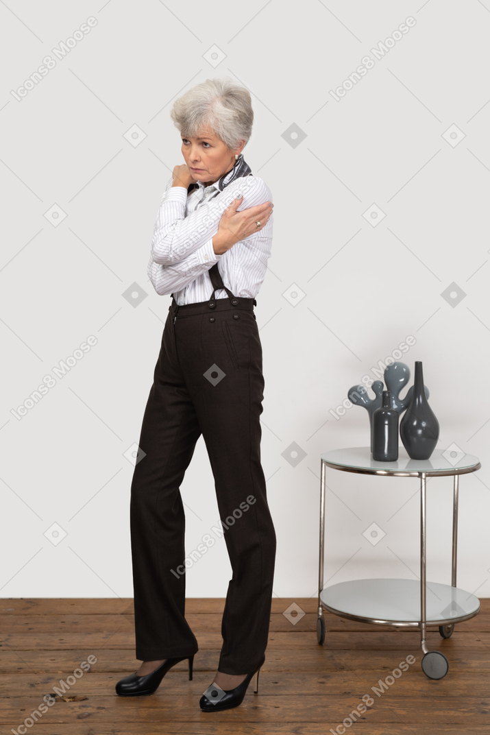 Three-quarter view of an old lady in office clothing embracing herself