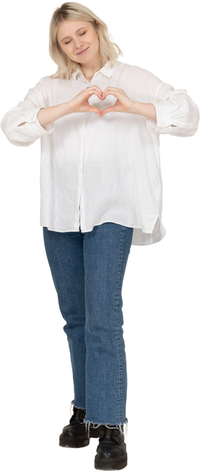 Vista frontal de una mujer rubia en ropa casual mostrando un gesto de corazón con los ojos cerrados