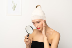 Young woman looking through magnifier and touching her cheek