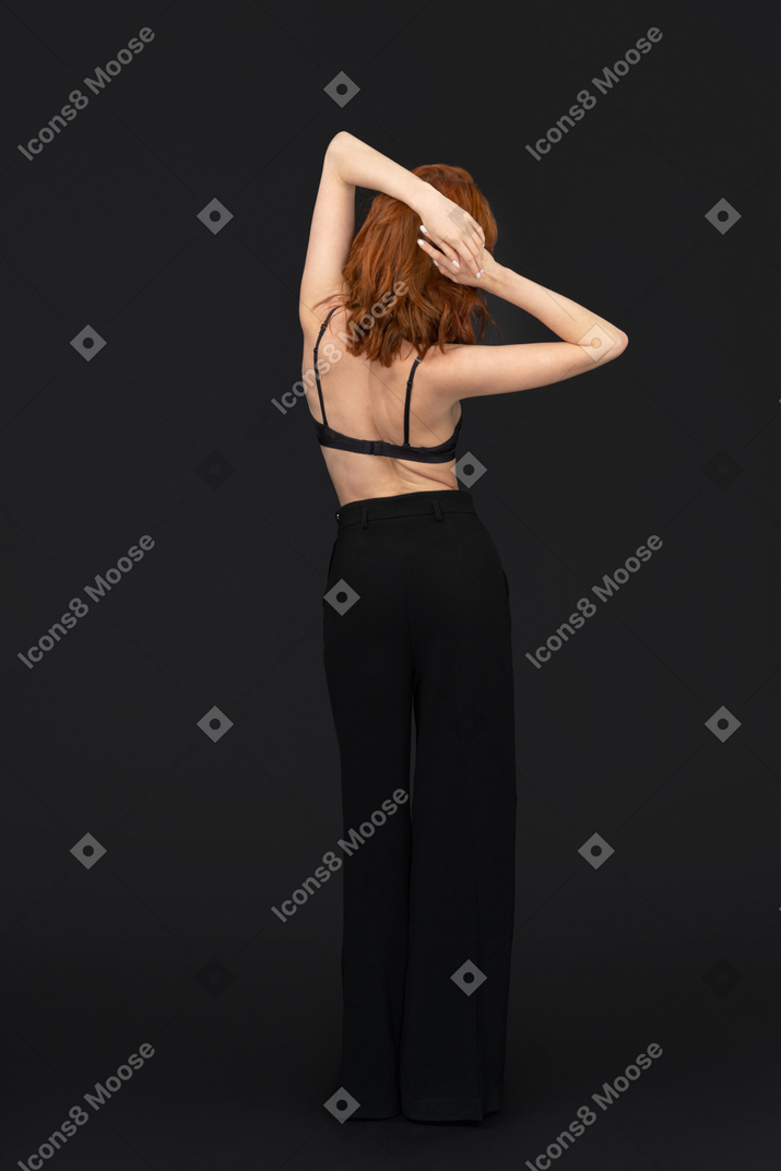 A backside of the pensive beautiful woman posing on the black background touching her hair