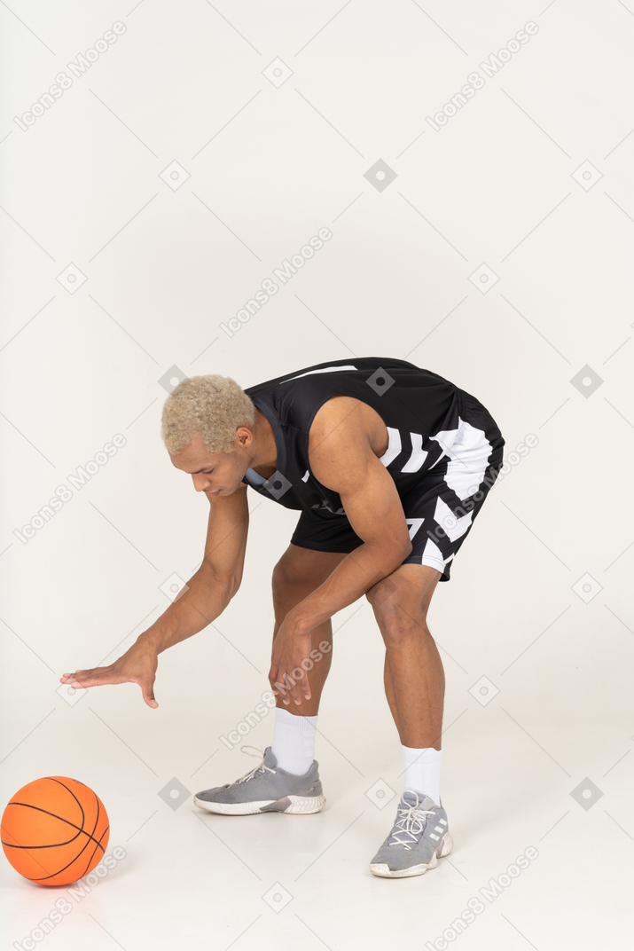 Vista di tre quarti di un giovane giocatore di basket maschile che tocca la palla