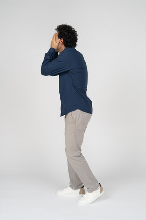 Side view of a man in casual clothes covering face with hands