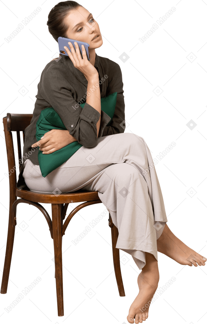 Vue de face d'une jeune femme assise sur une chaise tout en ayant un appel téléphonique