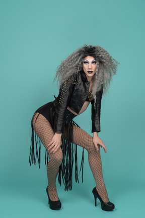 Drag queen in all black outfit leaning on bent knees